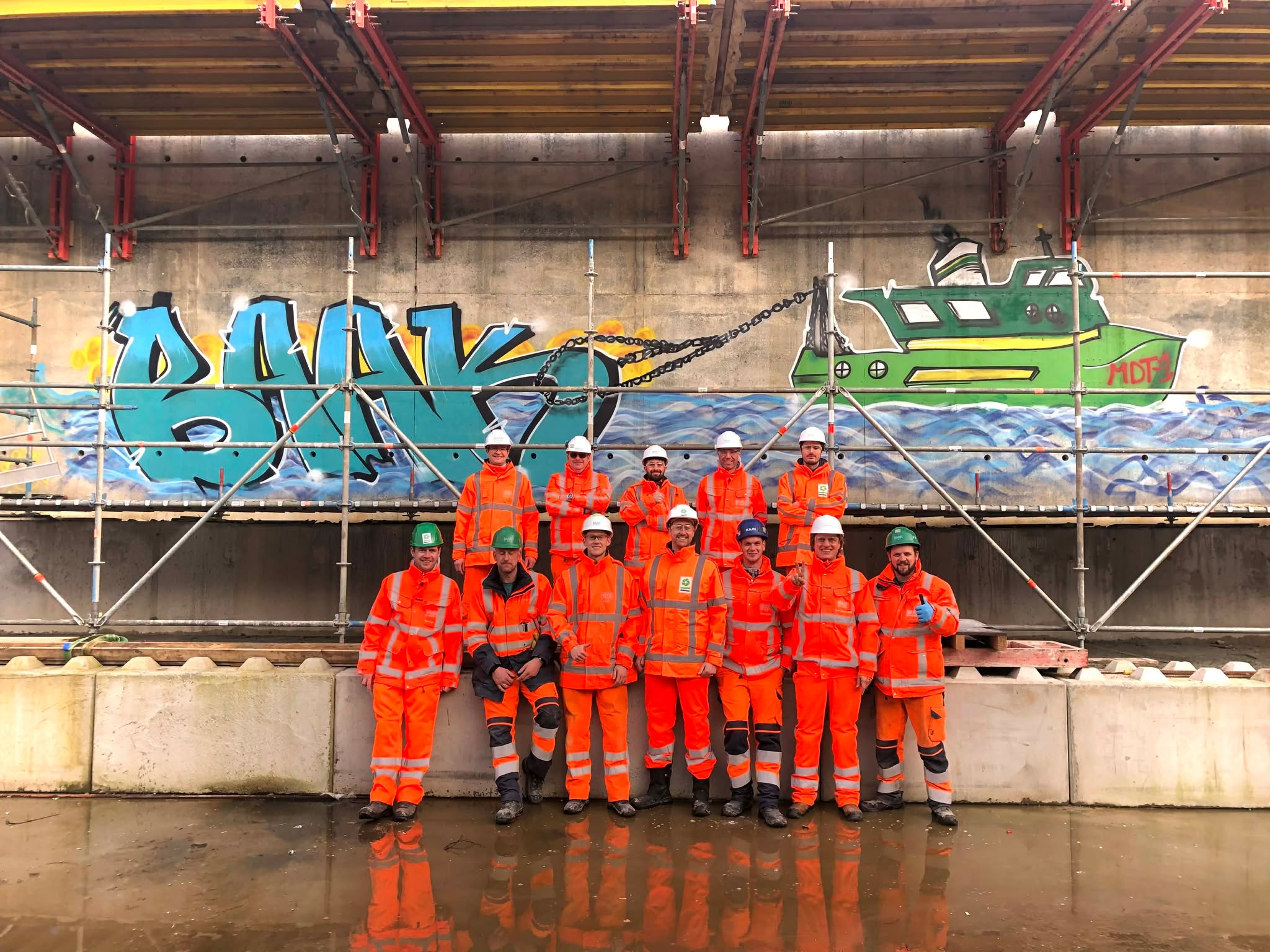 Colleagues in work gear in front of the graffiti mural they created together during a company outing