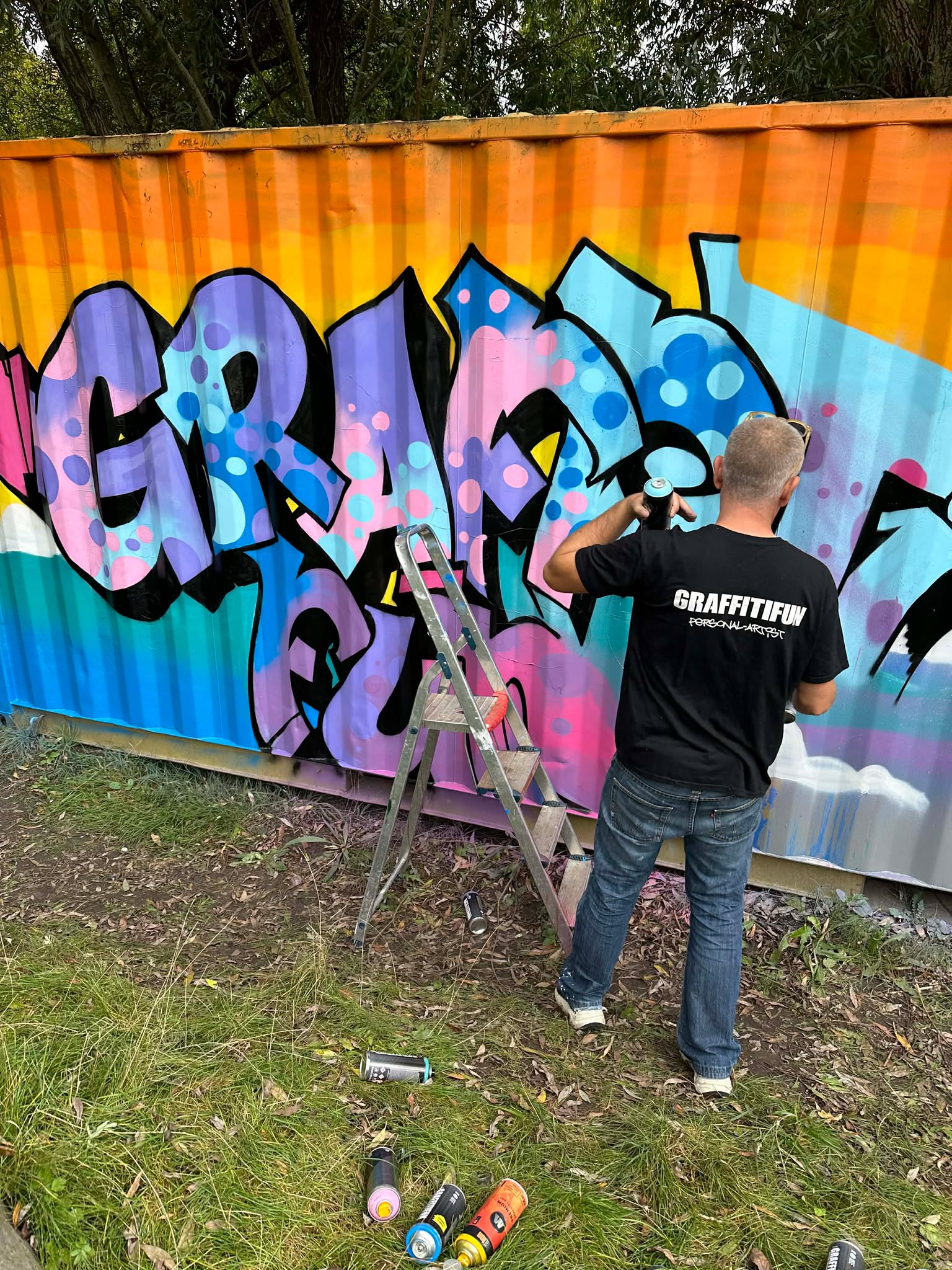 A Graffitifun artist painting a large colourful graffiti banner on a festival site